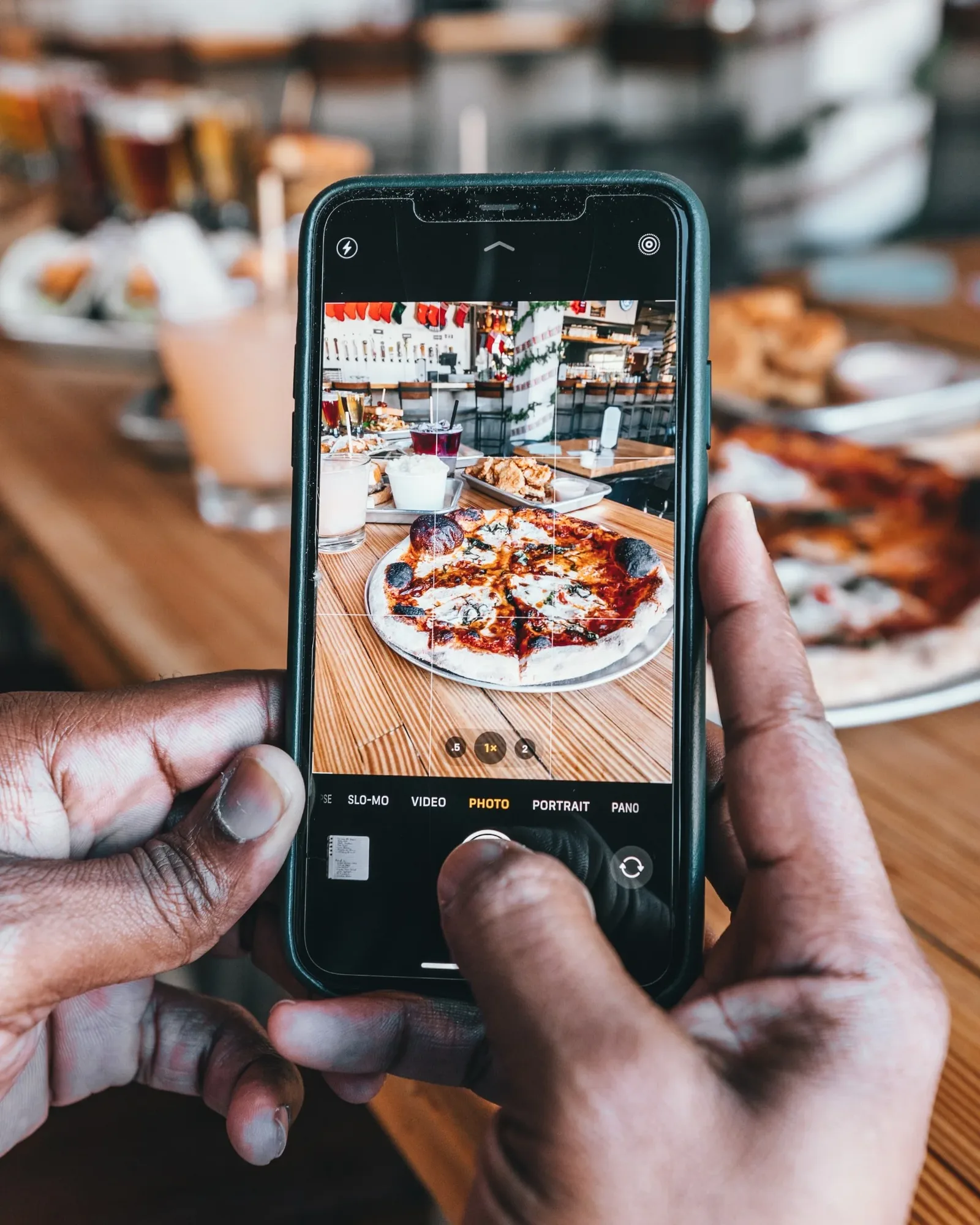 Customer photographing a pizza with a phone at a restaurant table