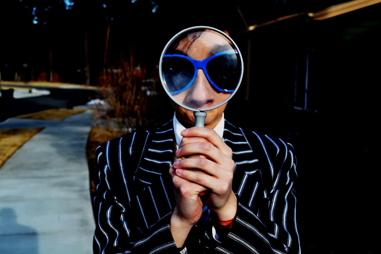 Person in sunglasses and a striped suit peering through a magnifying glass