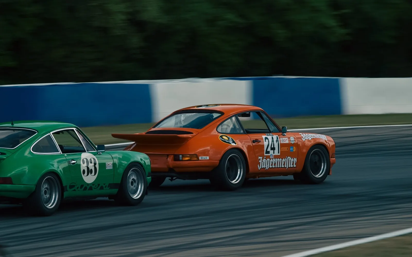 Two vintage Porsche race cars running nose to tail on a track, the trailing car drafting